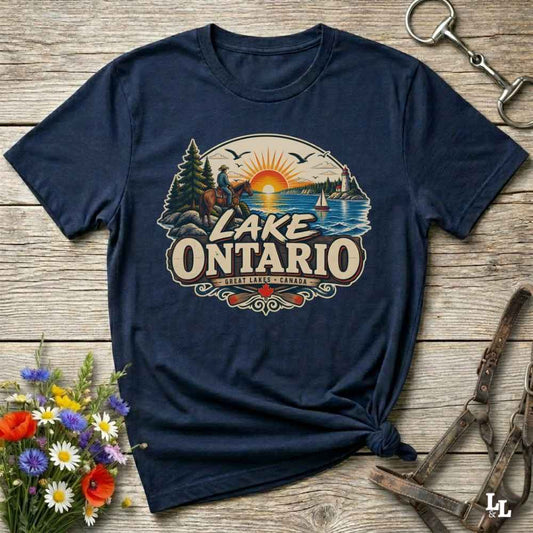 A navy blue short-sleeve t-shirt with a vintage-style 'Lake Ontario' graphic print, styled in a flat-lay on a rustic wooden background with decorative flowers and leather tack.