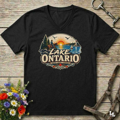 A black V-neck t-shirt with a colorful retro-style 'Lake Ontario' graphic, displayed flat on a rustic wooden background with equestrian and floral props.