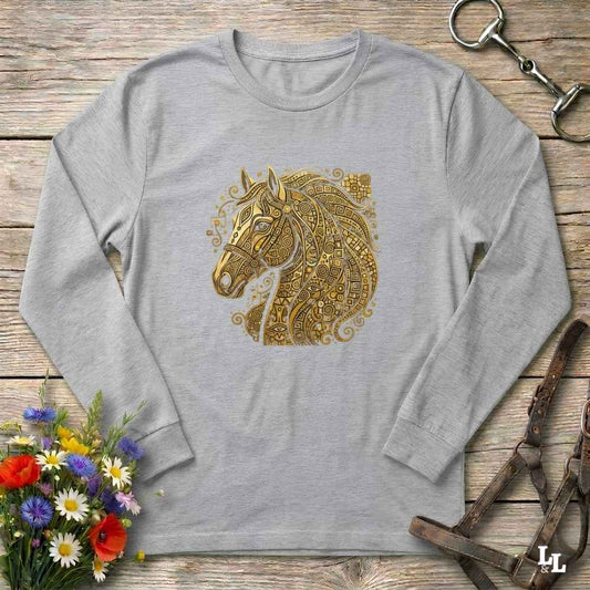 A light gray long-sleeve t-shirt with a detailed gold horse head graphic on the chest, styled in a flat-lay on a rustic wooden background with equestrian accessories and flowers.