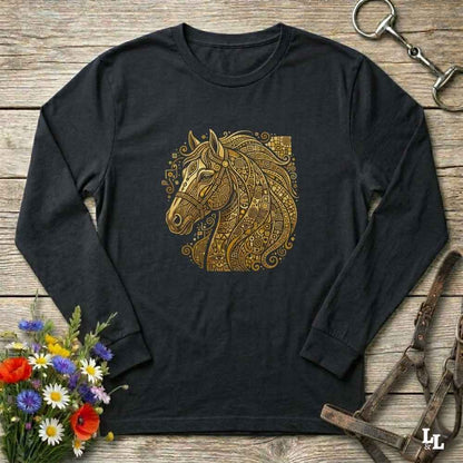 A black long-sleeve t-shirt with a detailed gold horse head graphic on the chest, styled in a flat-lay on a rustic wooden background with equestrian accessories and flowers.