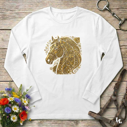 A white long-sleeve t-shirt with a detailed gold horse head graphic on the chest, laid flat on a rustic wooden surface with equestrian accessories and flowers.