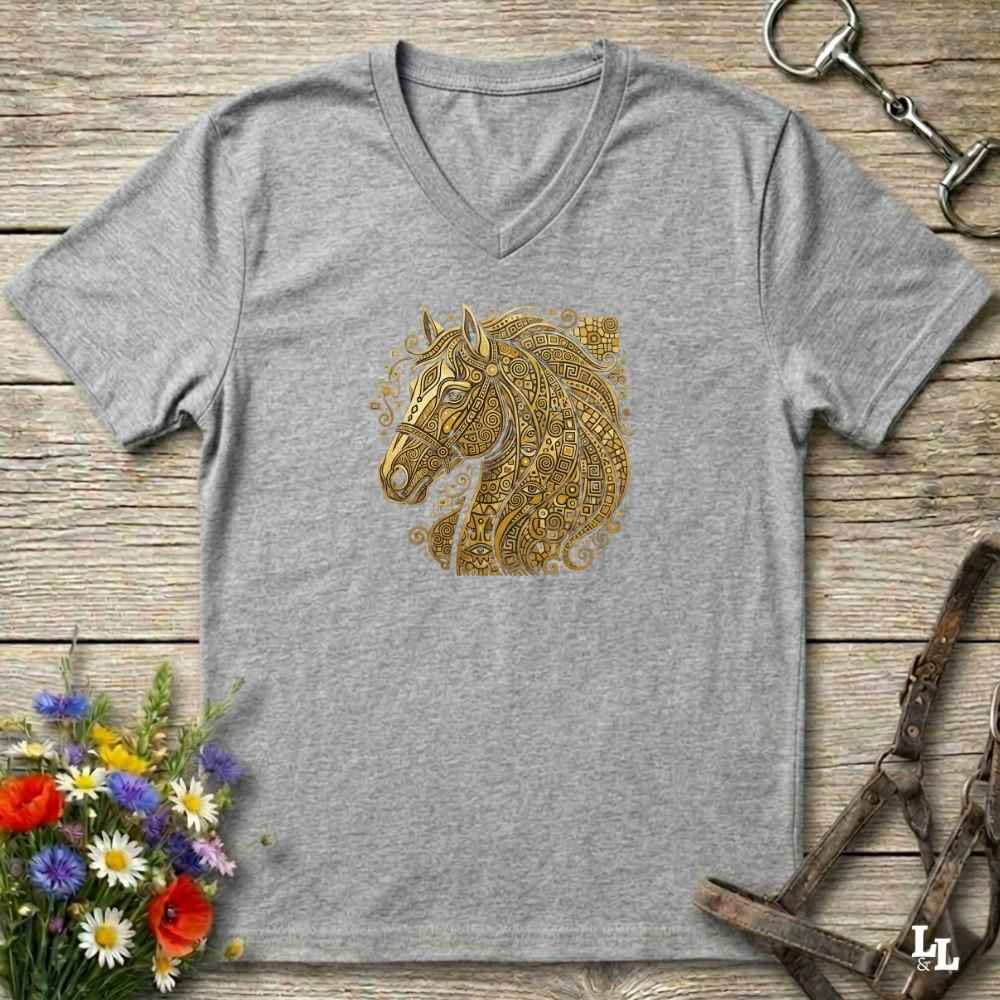 A heather gray V-neck t-shirt featuring a detailed gold horse head graphic on the chest, styled in a flat-lay on a rustic wooden background with equestrian accessories and flowers.