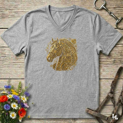 A heather gray V-neck t-shirt featuring a detailed gold horse head graphic on the chest, styled in a flat-lay on a rustic wooden background with equestrian accessories and flowers.
