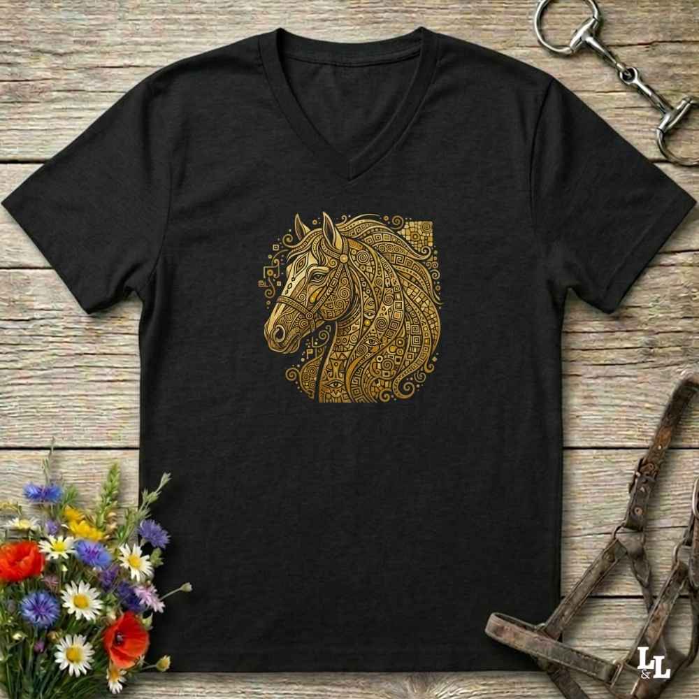 A black V-neck t-shirt featuring a detailed gold horse head graphic on the chest, styled in a flat-lay on a rustic wooden background with equestrian tack and flowers.