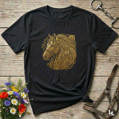 A black short-sleeve t-shirt with a detailed gold horse head graphic on the chest, styled in a flat-lay on a rustic wooden background with equestrian accessories and flowers.