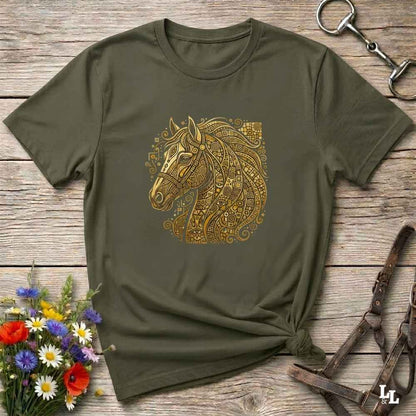 An olive green short-sleeve t-shirt with a detailed gold horse head graphic, styled in a flat-lay on a rustic wooden background with equestrian accessories and flowers.