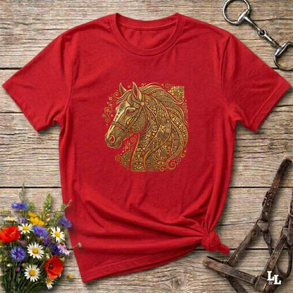 A red short-sleeve crewneck t-shirt featuring a detailed gold horse head graphic with intricate patterns, styled on a rustic wooden background with equestrian accessories and flowers.