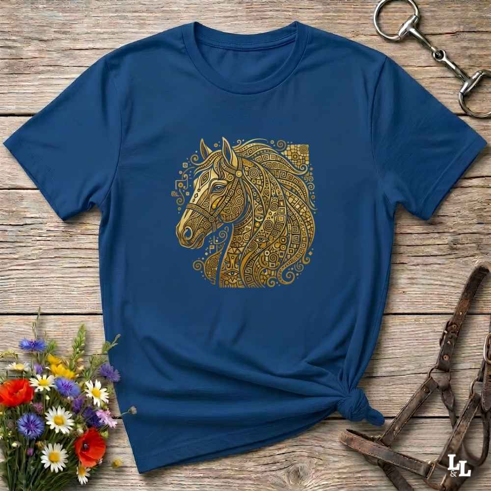 A navy blue short-sleeve t-shirt with a detailed gold horse head graphic on the chest, styled in a flat-lay on a rustic wooden background with equestrian and floral props.