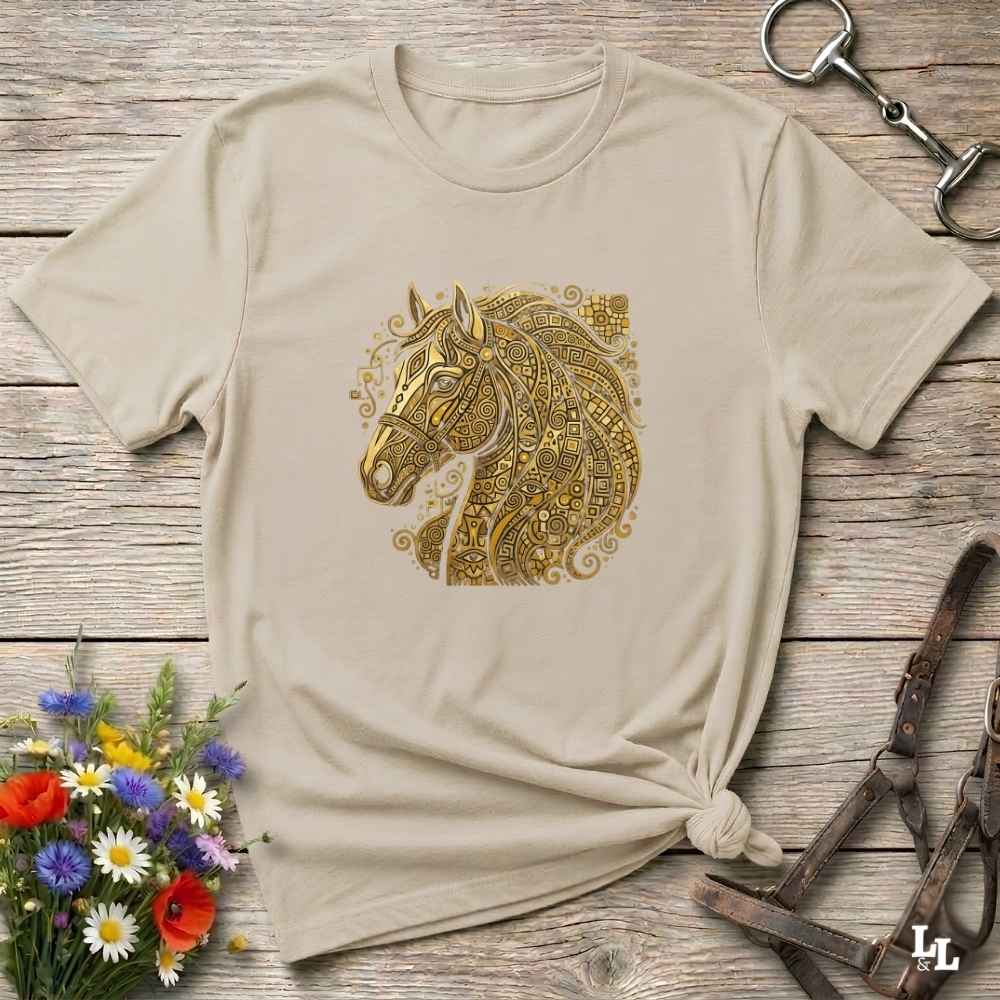 A beige short-sleeve t-shirt with a detailed gold horse head graphic on the chest, styled in a flat-lay on a rustic wooden background with equestrian accessories and flowers. Great gift.