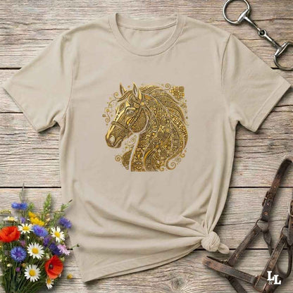 A beige short-sleeve t-shirt with a detailed gold horse head graphic on the chest, styled in a flat-lay on a rustic wooden background with equestrian accessories and flowers. Great gift.