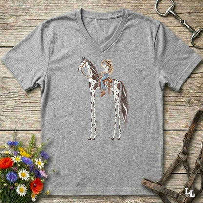 A heather gray V-neck t-shirt featuring a graphic of a woman riding a horse with long legs, styled in a flat-lay on a rustic wooden background with equestrian accessories and flowers.