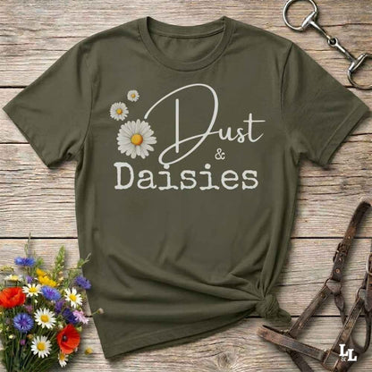 An olive green short-sleeve t-shirt with a 'Dust & Daisies' graphic, styled in a flat-lay on a rustic wooden background with a horse bit, leather halter, and a small bouquet of wildflowers.