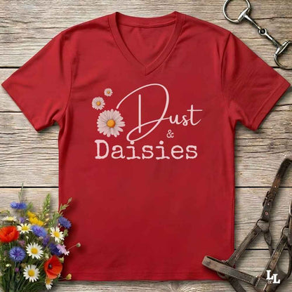 A red V-neck t-shirt with a white graphic reading 'Dust & Daisies' alongside daisy illustrations, laid flat on a rustic wood background with equestrian accessories and flowers around it.