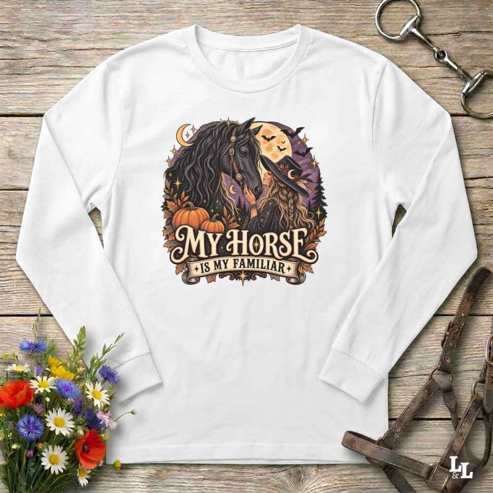 A white long-sleeve crewneck t-shirt with a graphic print of a woman and her horse, styled in a flat-lay on a rustic wooden background with equestrian accessories and flowers.