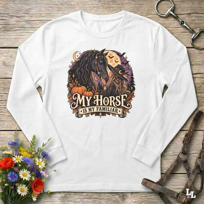 A white long-sleeve crewneck t-shirt with a graphic print of a woman and her horse, styled in a flat-lay on a rustic wooden background with equestrian accessories and flowers.
