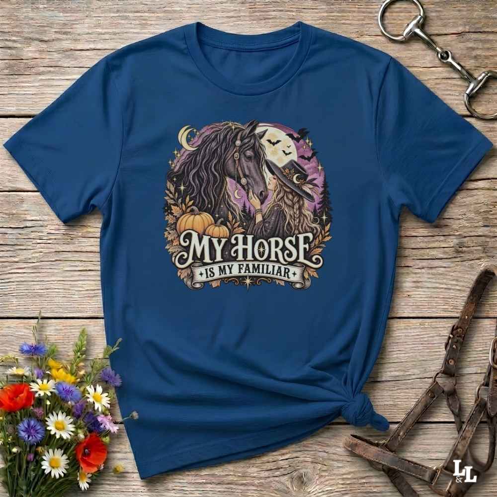A navy blue short-sleeve t-shirt with a graphic of two horses and the text 'MY HORSE IS MY FAMILIAR' in a fall-themed design, styled on a wooden surface with flowers and horse tack.