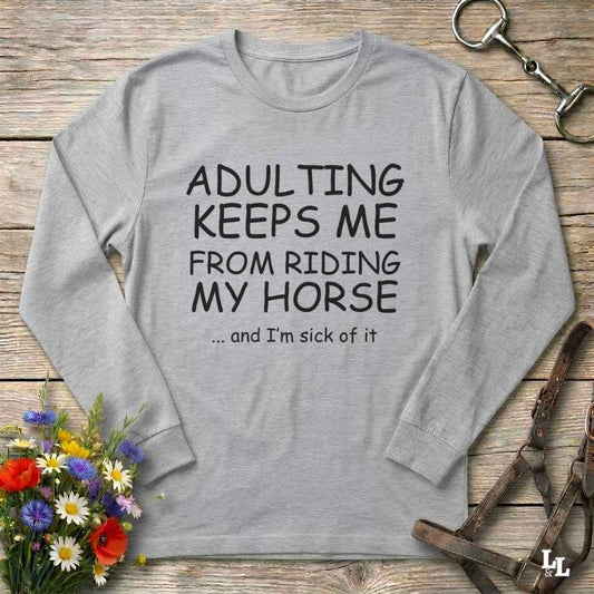 A light gray long-sleeve t-shirt with black printed text reading 'ADULTING KEEPS ME FROM RIDING MY HORSE .