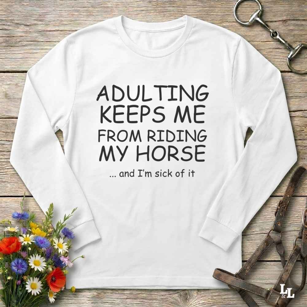 A white long-sleeve t-shirt with black printed text reading 'ADULTING KEEPS ME FROM RIDING MY HORSE .
