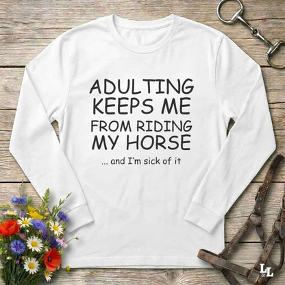 A white long-sleeve t-shirt with black printed text reading 'ADULTING KEEPS ME FROM RIDING MY HORSE .