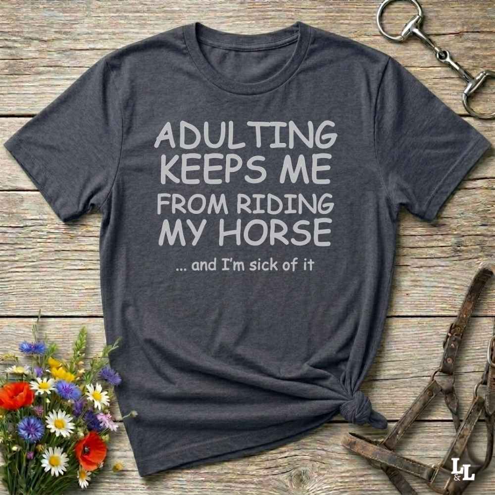 A dark charcoal gray graphic t-shirt with white text reading 'ADULTING KEEPS ME FROM RIDING MY HONSE .