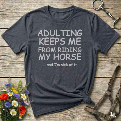 A dark charcoal gray graphic t-shirt with white text reading 'ADULTING KEEPS ME FROM RIDING MY HONSE .