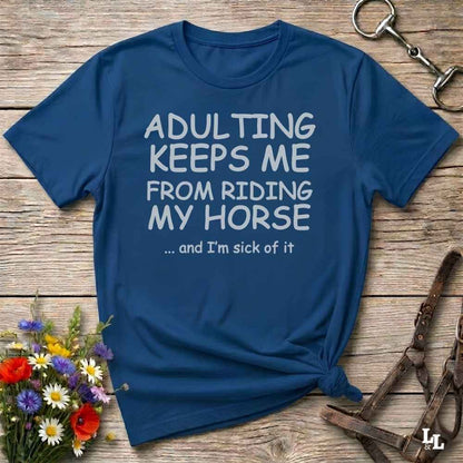 A navy blue graphic t-shirt with white text reading 'ADULTING KEEPS ME FROM RIDING MY HORSE .