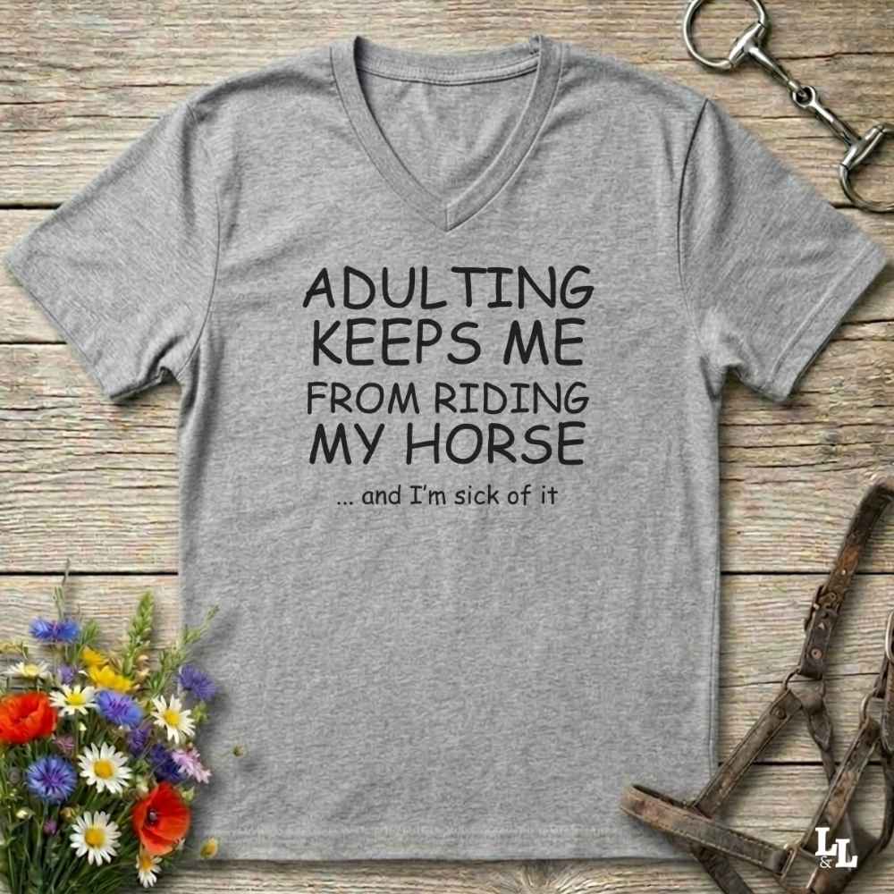 A heather gray V-neck t-shirt with black text reading 'ADULTING KEEPS ME FROM RIDING MY HORSE .