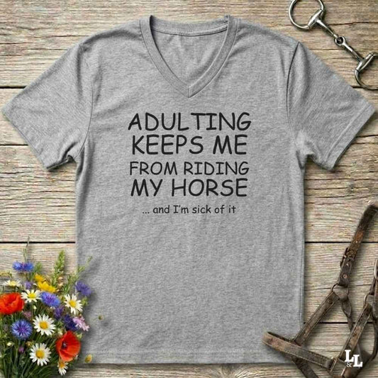 A heather gray V-neck t-shirt with black text reading 'ADULTING KEEPS ME FROM RIDING MY HORSE .