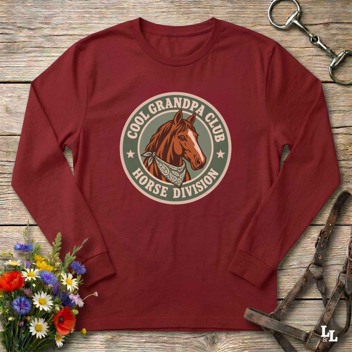 A long-sleeve crewneck t-shirt in maroon red, laid flat on a rustic wooden surface. The shirt features a circular graphic print in the center with a brown horse illustration and the text 'COOL GRANDPA CLUB HORSE DIVISION'.