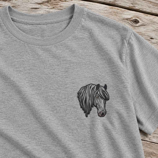 A close-up of a light heather gray crewneck t-shirt featuring a small black and gray graphic of a horse's head on the left chest, laid flat on a rustic wooden surface.