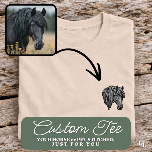A folded beige t-shirt displayed on a rustic wood background, featuring a black horse graphic on the chest and a green banner at the bottom that reads 'Custom Tee YOUR HORSE or PET STITCHED. JUST FOR YOU.