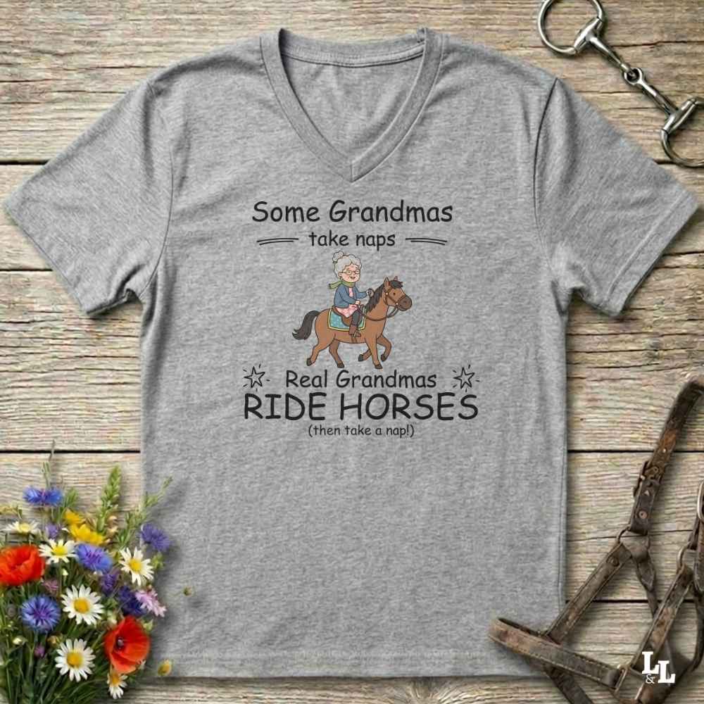 A heather gray V-neck t-shirt with a graphic print of a grandma riding a horse, displayed on a rustic wooden background with equestrian accessories and flowers.