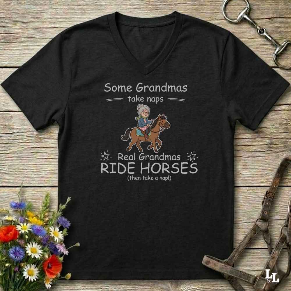 A black V-neck t-shirt with a humorous equestrian graphic for grandmas, laid flat on a rustic wooden background with equestrian props and flowers.