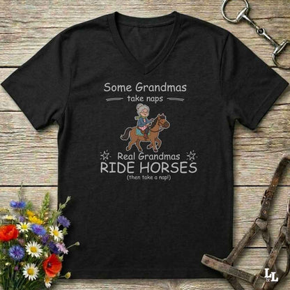 A black V-neck t-shirt with a humorous equestrian graphic for grandmas, laid flat on a rustic wooden background with equestrian props and flowers.