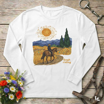 A white long-sleeve t-shirt with a colorful 'Gogh riding' landscape graphic, laid flat on a rustic wooden surface with equestrian and floral props.