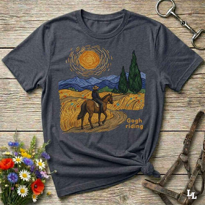 A dark heather gray t-shirt with a graphic print of a rider on a horse in a Van Gogh-inspired landscape, styled on a rustic wooden background with equestrian accessories and flowers.