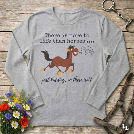 A light gray long-sleeve t-shirt with a humorous horse graphic and text, displayed in a flat-lay arrangement on a rustic wooden background with flowers and equestrian accessories.