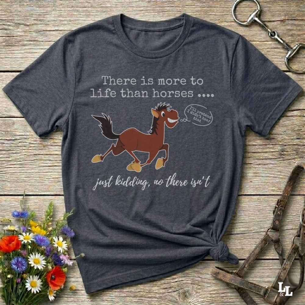 A dark heather gray graphic t-shirt laid flat on a rustic wooden background, styled with horse accessories and a small bouquet of wildflowers. The shirt features a cartoon illustration of a brown horse with a speech bubble t