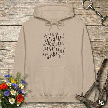 A beige pullover hoodie with a black pine tree forest graphic on the chest, laid flat on a rustic wooden surface with flowers and horse tack props.