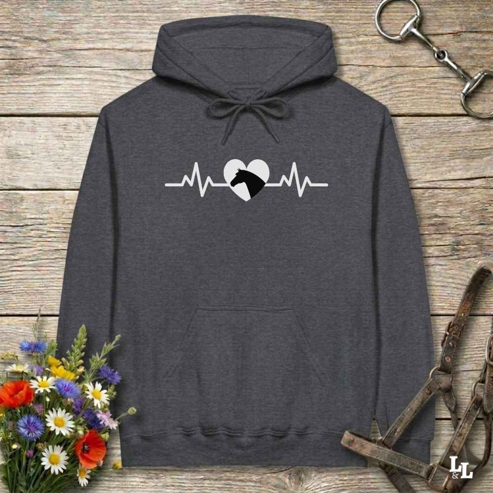 Dark gray hoodie with text Heartbeat line and a horse head, on wooden background with equestrian bit and halter and flowers