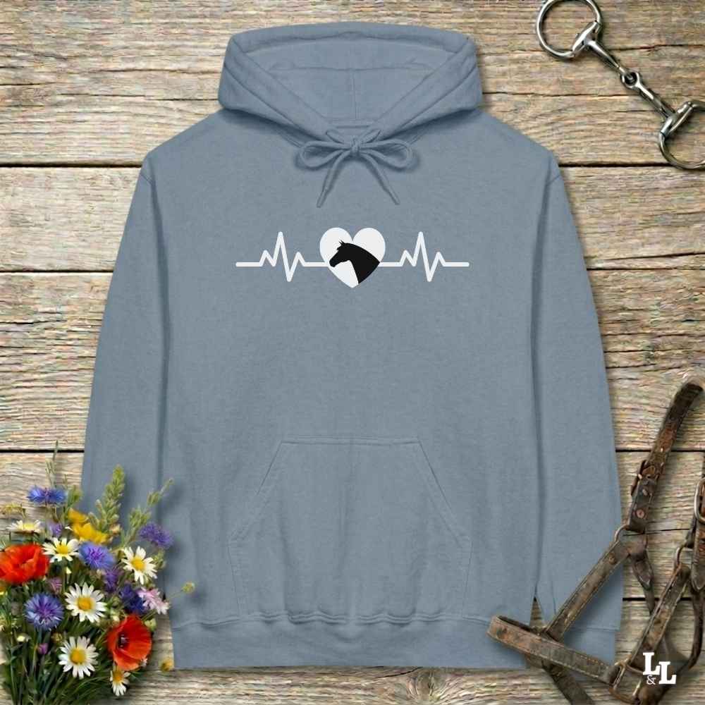 Blue hoodie with text Heartbeat line and a horse head, on wooden background with equestrian bit and halter and flowers