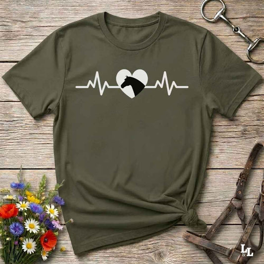 Green t-shirt with heartbeat line and horse head in the middle of the heart, on wooden background with flowers and equestrian bit and halter