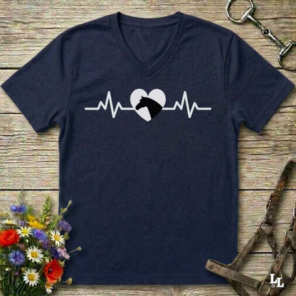 A navy blue V-neck t-shirt with a white heartbeat line graphic and a black horse head inside a white heart, laid flat on a rustic wooden surface with decorative flowers and horse tack.