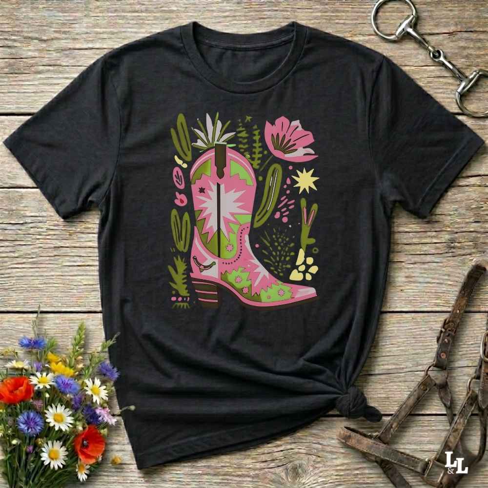 Bright pink and green cowgirl boot printed on a unisex western t-shirt, styled for a boho country vibe. The design is surrounded by floral and cactus illustrations to enhance the desert western theme.