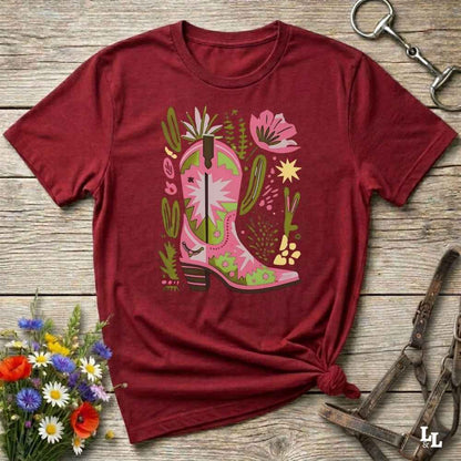 Bright pink and green cowgirl boot printed on a unisex western t-shirt, styled for a boho country vibe. The design is surrounded by floral and cactus illustrations to enhance the desert western theme.