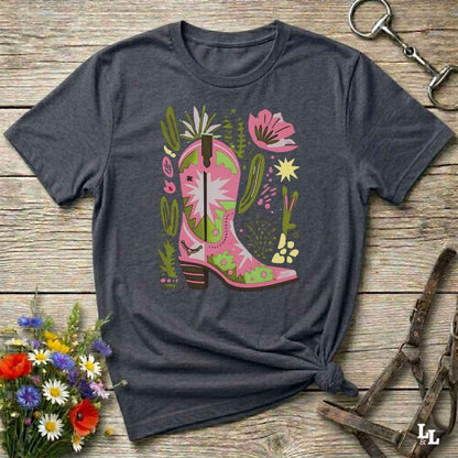 Bright pink and green cowgirl boot printed on a unisex western t-shirt, styled for a boho country vibe. The design is surrounded by floral and cactus illustrations to enhance the desert western theme.