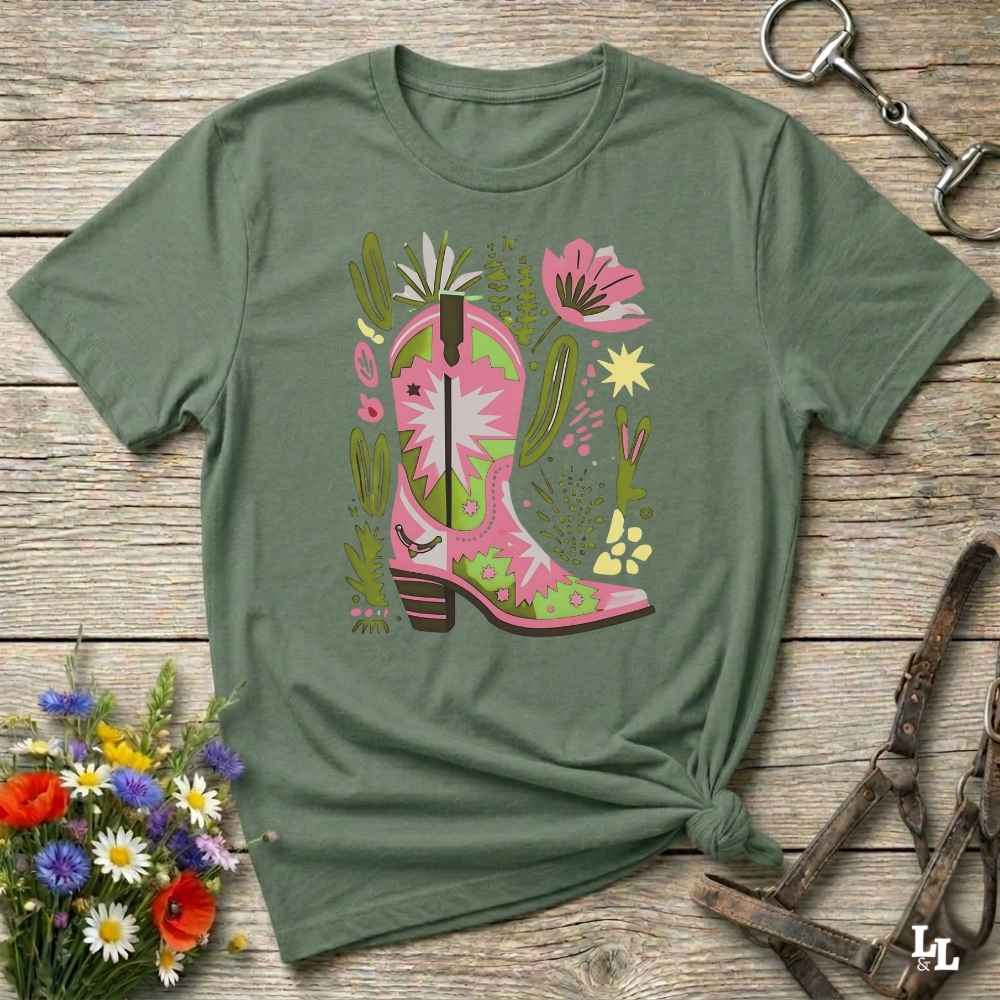 Bright pink and green cowgirl boot printed on a unisex western t-shirt, styled for a boho country vibe. The design is surrounded by floral and cactus illustrations to enhance the desert western theme.