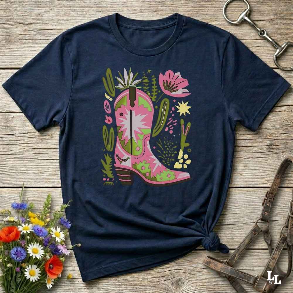 Bright pink and green cowgirl boot printed on a unisex western t-shirt, styled for a boho country vibe. The design is surrounded by floral and cactus illustrations to enhance the desert western theme.