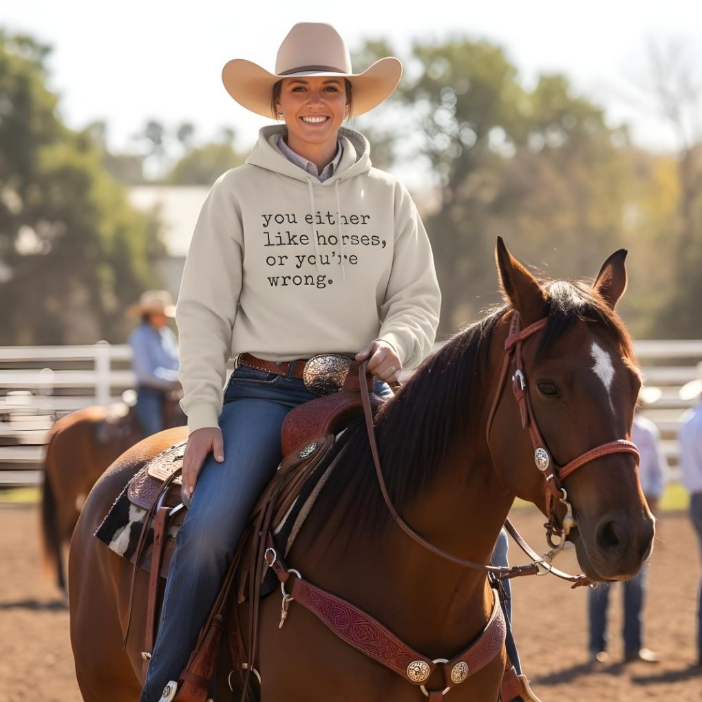 Person riding a horse wearing a hoodie with text, with a blurred background of people and trees. You Either Like Horses or You're Wrong Hoodie for Horse Riders, Trail Riding Sweatshirt