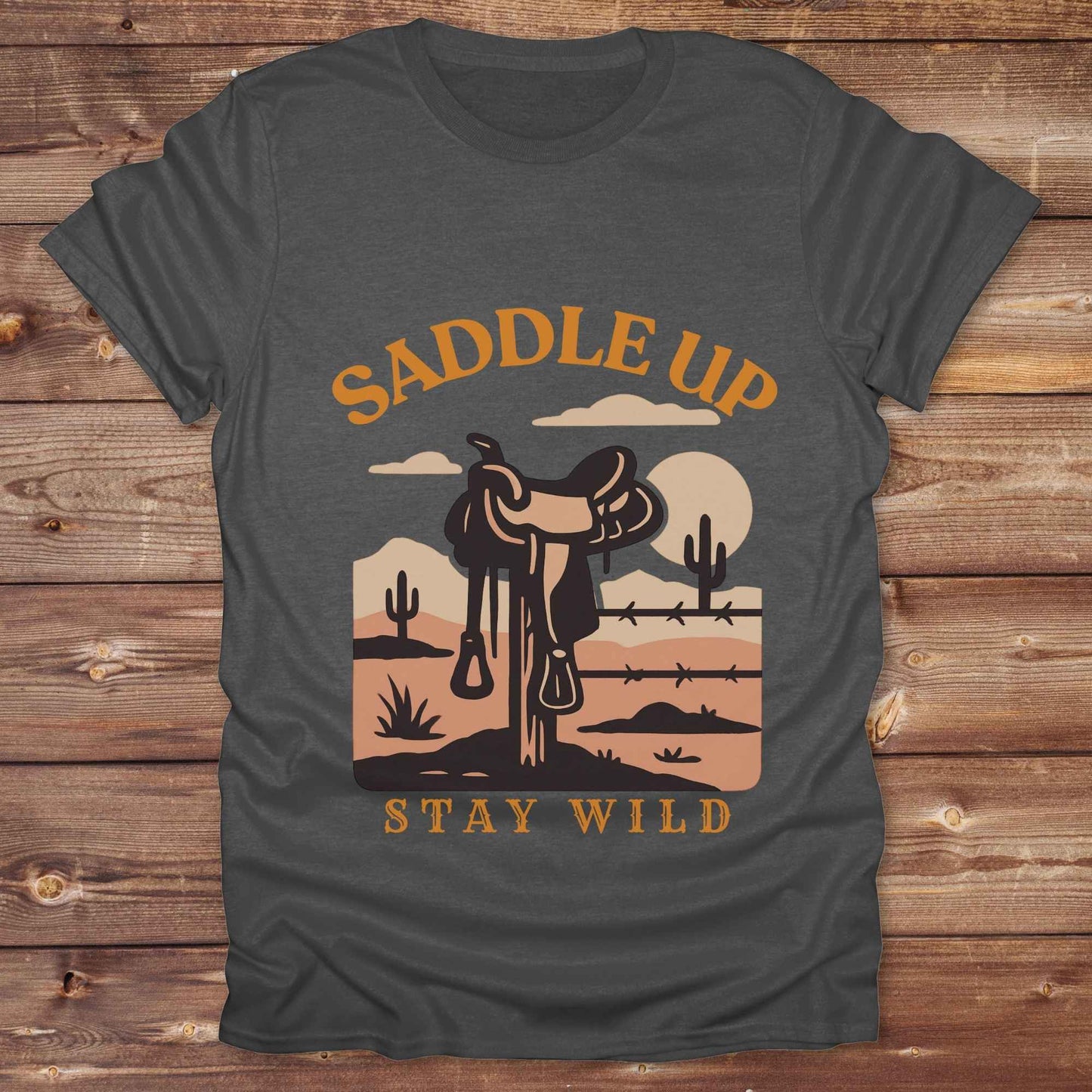 Saddle Up Stay Wild western t-shirt features a bold desert sunset graphic with a classic saddle and western landscape. Perfect for cowgirls, cowboys, and horse lovers, this rustic tee blends adventure with comfort and country charm. Whether you're heading to a rodeo, trail ride, or simply embracing your wild side, this shirt offers a soft fit and bold design. Designed for western wear fans, equestrians, and country souls, it's a must have for anyone who lives the saddle life. 